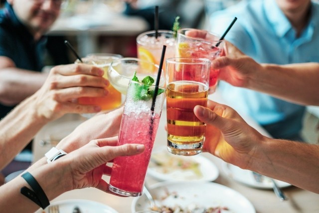 Photo en gros plan sur les mains d'un groupe de personnes trinquant avec des verres et boissons variées.